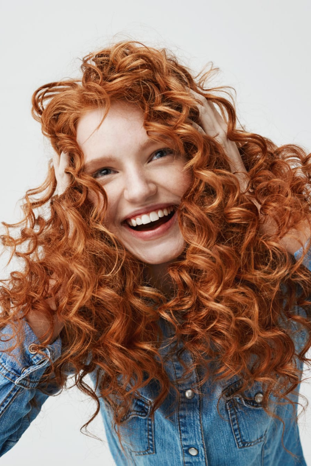 Just Wild Care ürünleri ile belirginleşmiş, hacimli ve sağlıklı kızıl kıvırcık saçlara sahip gülen kadın.